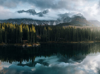 Aerial view of serene lake reflecting majestic mountains and lush forests under cloudy skies, Dolomites, Provinz Belluno, Italy.