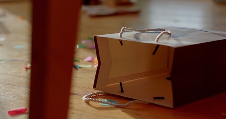A colorful shopping bag is carelessly left on the floor, surrounded by scattered, vibrant confetti that adds a festive touch to the scene