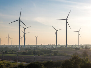 Obraz premium Hundred of wind turbines standing in agricultural rural field generating green ecological energy at Huay Bong, Thailand