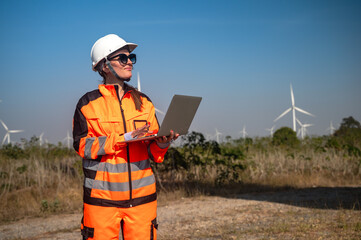 Female Caucasian wind turbine engineer in safety uniform and helmet holding taplet working in outdoor turbine field
