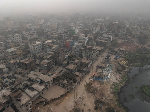 Aerial view of a foggy and hazy urban landscape with crowded buildings and streets alongside a river, Lalbagh Thana, Dhaka, Bangladesh.