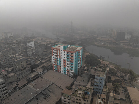 Aerial view of densely populated urban landscape with apartment buildings and a river under foggy and overcast skies, Lalbagh Thana, Dhaka, Bangladesh.