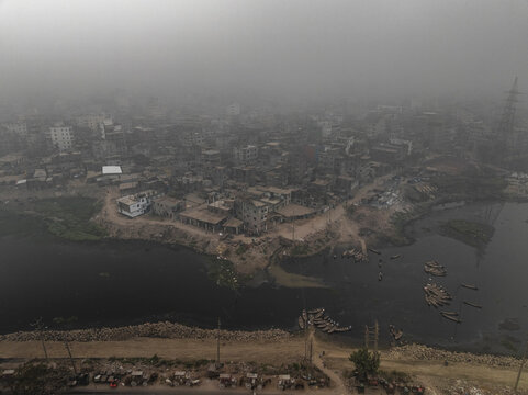 Aerial view of foggy Buriganga river with dense buildings and boats along the shoreline, Lalbagh Thana, Dhaka, Bangladesh.
