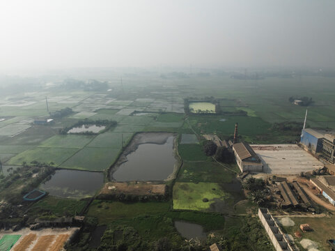 Aerial view of green rice fields and ponds with buildings and factory, Uttar Panisar, Sarail, Chattogram, Bangladesh.