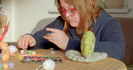 A young child is deeply focused on crafting with an array of colorful supplies spread out across a...