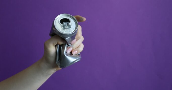 Woman crushing aluminium can on purple background, closeup. Space for text