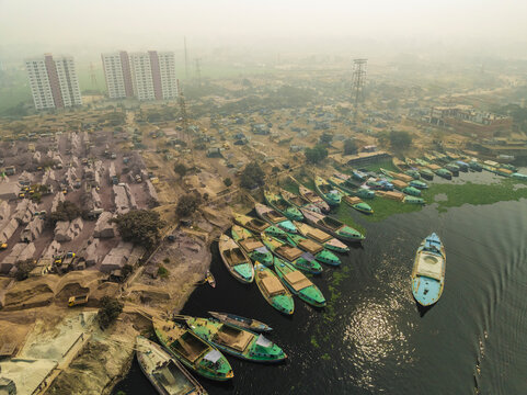 Aerial view of boats on Buriganga river with cement industries and urban buildings, Amin Bazar, Savar, Dhaka, Bangladesh.