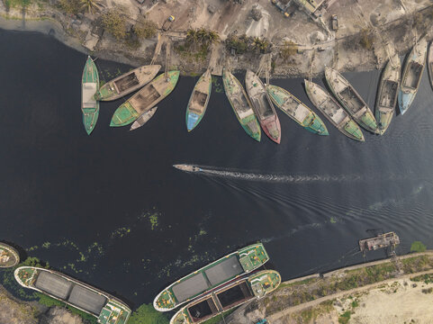 Aerial view of traditional boats on the Buriganga river with cement industries in the background, Amin Bazar, Savar, Dhaka, Bangladesh.