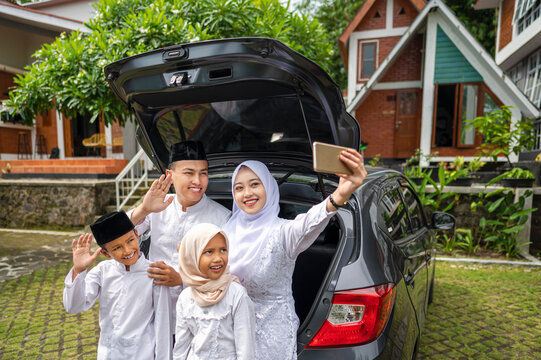 Indonesian Muslim family with mobile phone take selfie or video call before mudik or traveling to their hometown. Concept of Happy Lebaran, Eid Al Fitr, Idul Fitri, and Ramadan Mubarak celebration