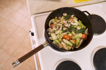 Chopped vegetables with spices are stewed in a pan on the stove in the kitchen