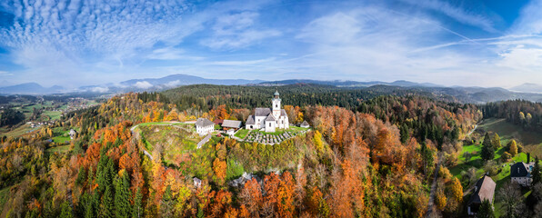 Aerial view of a beautiful autumn landscape with a historic church and chapel on a hill surrounded by colorful foliage and tranquil forest, Sternberg, Carinthia, Austria.