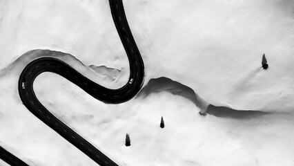 Aerial view of cars tackling the treacherous winding road through a snowy landscape with trees, Julier Pass, Graubuenden Canton, Switzerland.