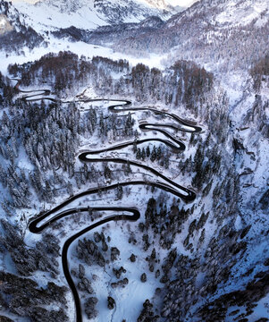 Aerial view of winding road through a snowy landscape with many little cars navigating the treacherous route, Maloja Pass, Graubuenden Canton, Switzerland.