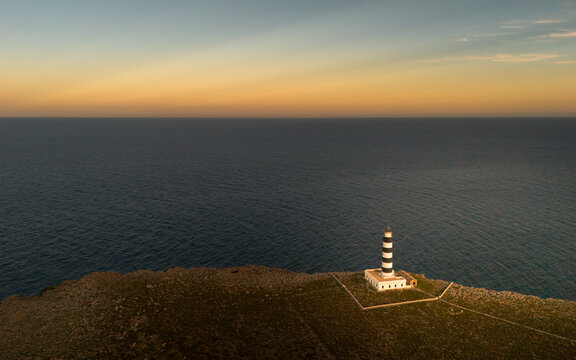 Aerial view of the picturesque Cap de l'Isla de l'Aire lighthouse at sunset over the tranquil sea and coastline, Punta Prima, Menorca, Balearic Islands, Spain.
