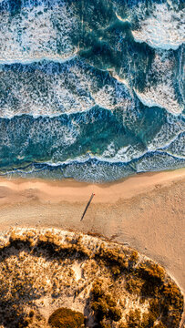 Aerial view of serene beach with man's shadow looking towards the calm sea and crashing waves, Son Bou, Balearic Islands, Spain.