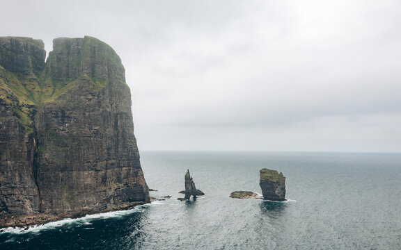 Aerial view of the majestic Risin og Kellingin rock formations on a rugged coastline with dramatic cliffs and a serene ocean, Eidi, Eysturoy, Faroe Islands.