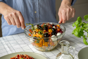Women's hands mix salad with tomato tomato mozzarella vegetables and arugula in a large bowl for an easy diet lunch or dinner, a healthy balanced meal	