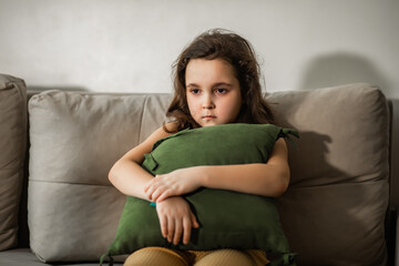 Obraz premium Child sitting alone on sofa feeling stressed unhappy, sad and depress. Little girl embracing pillow.