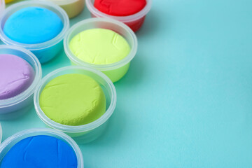 Different colorful modeling clay in plastic jars on light blue background, closeup. Space for text