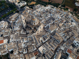 Aerial view of the beautiful Church of Saint George Martyr surrounded by historic medieval buildings and picturesque rooftops, Locorotondo, Bari, Italy.