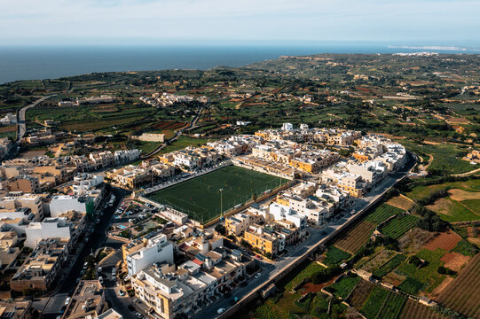 Aerial view of a scenic football field surrounded by residential buildings and lush greenery, Dingli, Malta.