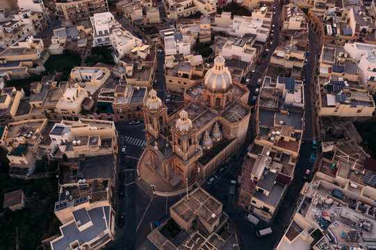 Aerial view of rotunda St. John Baptist Church amidst historic stone buildings and rooftops, Dingli, Malta.