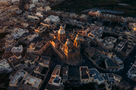 Aerial view of rotunda st john baptist church surrounded by historic buildings and picturesque rooftops at sunset, Dingli, Malta.