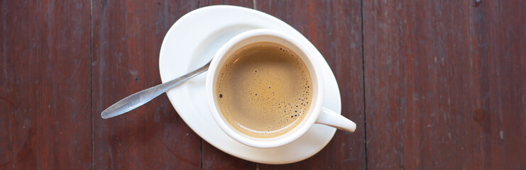 Panorama view porcelain Espresso coffee cup with saucer and stainless-steel spoon on wooden table at local coffee shop in Can Tho, Southern Vietnam, top view single hot drink with copy space