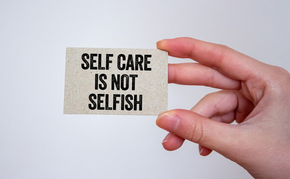 Self care is not selfish message written on a card in hand. Conceptual self care is not selfish symbol. Copy space.