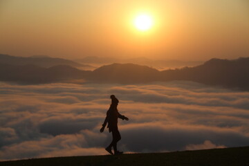 silhueta de mulher em topo de montanha com mar de nuvens e sol nascendo no horizonte - foto tirada no morro são bernardo em rio dos cedros, santa catarina 
