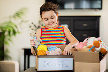 Cute teenager kid girl packing cuddly toys in the donation box at home.