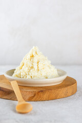 Unrefined shea butter in a bowl with wooden spoon on a board. Vertical orientation.
