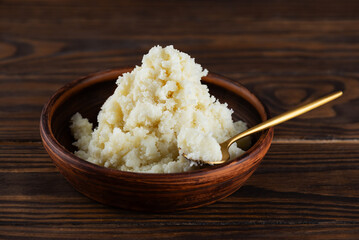 Unrefined shea butter and golden spoon in a clay plate on wooden table.