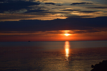 Sunset Over the Ocean, Sea with Colorful Orange Sky, Reflections Rocky Shoreline. Sky with warm colors as the golden hour casts a stunning reflection on the sea water.  Vacation spot for relaxation. 