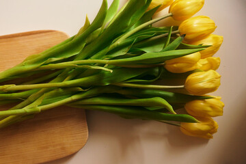 A beautiful arrangement of spring flowers. Yellow tulips are lying on a white table on a wooden board. Care of cut flowers at home, pruning stems