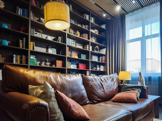 Cozy reading nook featuring a leather sofa and well-stocked bookshelf in a sunlit room
