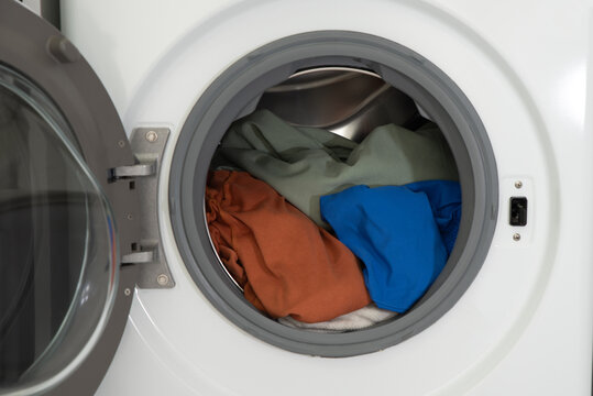 Colored items in a white washing machine with an open door in the laundry room for cleaning.