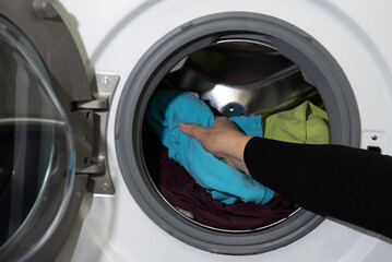 modern woman puts dirty clothes in a white washing machine with an open door in the laundry room for cleaning.