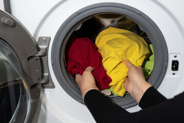 modern woman puts dirty clothes in a white washing machine with an open door in the laundry room for cleaning.
