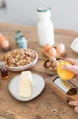 In a cozy kitchen, preparations for baking are underway as hands zest a lemon, surrounded by butter, eggs, and natural ingredients, exuding a warm, inviting atmosphere for wholesome cooking