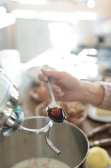 In a cozy farmhouse kitchen, a hand delicately pours homemade vanilla essence into a mixing bowl, surrounded by fresh ingredients and the aroma of baking