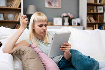 Attractive woman freelancer worker using digital tablet sitting at cozy sofa in living room. Successful businesswoman text message in home. Online technology concept, remote job e-commerce e-learning. © Srdjan