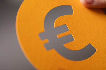 Close-up of a euro symbol cut from orange paper. Finance, currency, money concept.