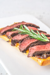 Grilled ciabatta sandwich with melted cheese, juicy steak, caramelized onions, and rosemary