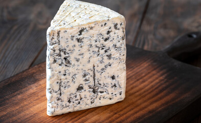 Wedge of Roquefort cheese resting on a rustic wooden cutting board