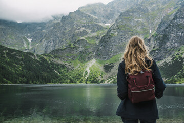 Blonde woman looking at a beautiful view with a lake in the high mountains in Poland. The Morskoye Oko lake