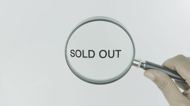 Sold out text or word highlighted by a magnifying glass in a hand on a white background, symbolizing focus on product availability, scarcity, and finalization of sales