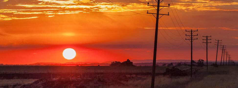 The setting sun sinks through smoke haze along side  a long row of power poles