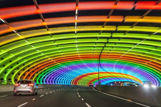 A car driving through a tunnel lit with rainbow coloured lights