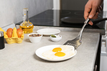 Man with frying pan putting tasty fried eggs onto plate in kitchen, closeup